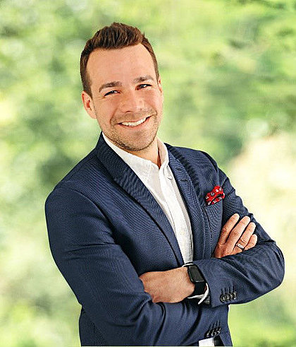 Lächelnder Mann im Anzug mit verschränkten Armen vor grüner Kulisse